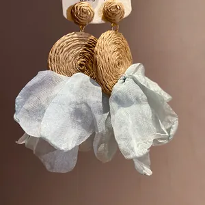 Primer plano de pendientes boho de rafia con pétalos de gasa azul en tarjeta.