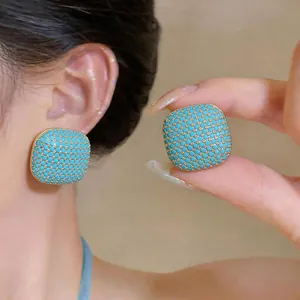 Detail of square turquoise stud earrings with gold grid pattern on ear and hand.