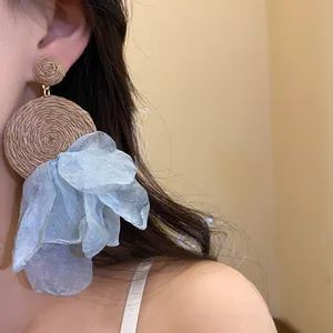 Detalle de pendientes colgantes de rafia con pétalos de gasa azul de estilo bohemio