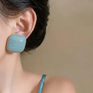 Close-up of square geometric stud earring with blue textured inlay and gold border
