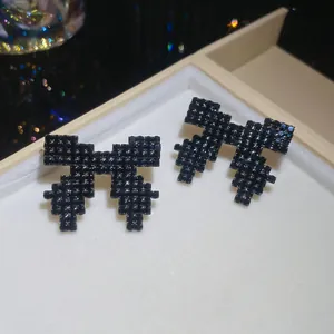 Detail view of black rhinestone pixelated bow earrings placed in a cream jewelry box