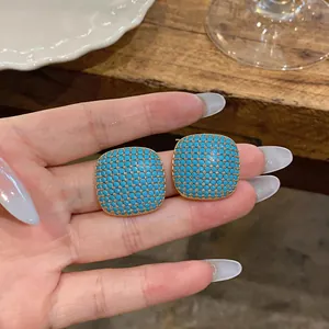 Detailed view of square geometric stud earrings with blue stone inlay and gold finish