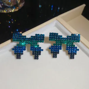 Macro detail of pixel-art bow earrings featuring blue and green rhinestone gradient