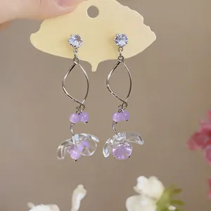 Dettaglio di orecchini in zircone con perline viola e pendenti floreali in acrilico trasparente
