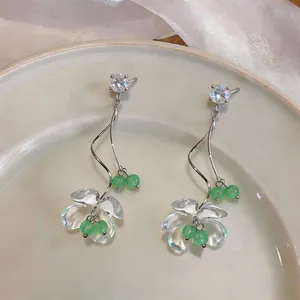 Primo piano di orecchini pendenti con fiori in acrilico e zirconi e perle verdi su piatto