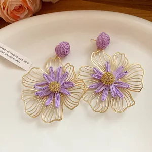 Macro view of purple raffia flower earrings with intricate gold wireframe detailing.