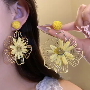 Detailed view of large yellow raffia flower earrings with gold-toned metal accents.