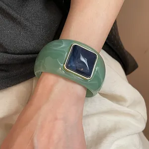 Primer plano detallado de un brazalete de acrílico mármol verde con pieza central azul.