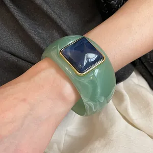 Primer plano de brazalete de acrílico verde con piedra cuadrada morada y oro.