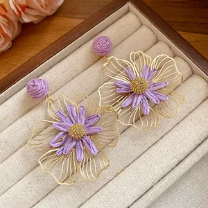 Close-up detail of purple raffia and gold hollow floral earrings on a velvet tray