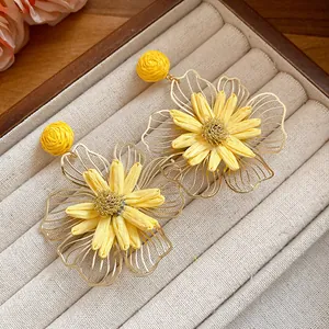 Close-up detail of vibrant yellow raffia flower earrings with gold-toned petals
