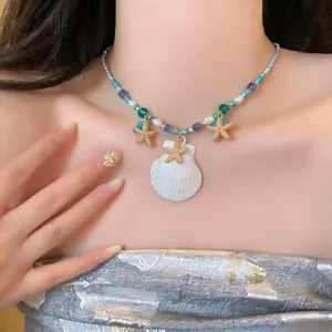 Gros plan d'un collier de perles avec coquillage blanc et étoiles de mer dorées sur un mannequin