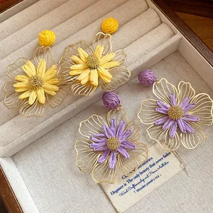 Detailed view of yellow and purple raffia flower earrings with hollow metal petal outlines.