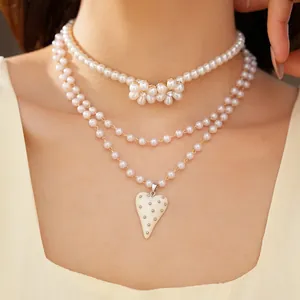Détail d'un collier de perles multicouche avec breloques fleurs et pendentif cœur.