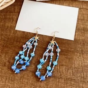 Gros plan de boucles d'oreilles en perles bleues avec étoiles de mer dorées sur bois.