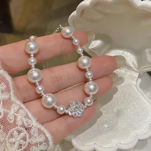 Close-up of pearl bracelet featuring a silver camellia flower charm and elegant pearls.
