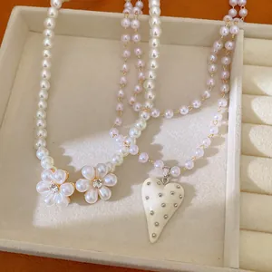 Détail de colliers en perles élégants avec fleurs nacrées et un pendentif coeur clouté
