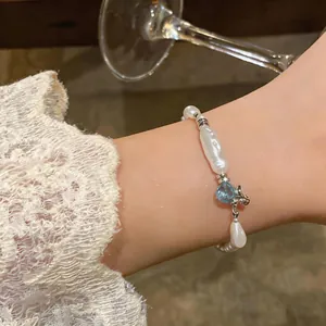 Detail view of a French style irregular pearl bracelet with a blue heart charm on a wrist