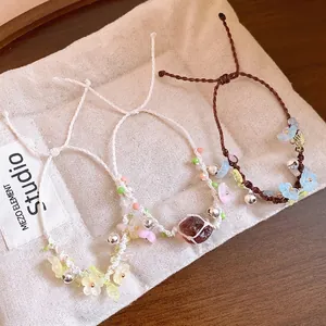 Bracelets faits main avec fleurs en résine et clochettes sur une pochette en tissu crème