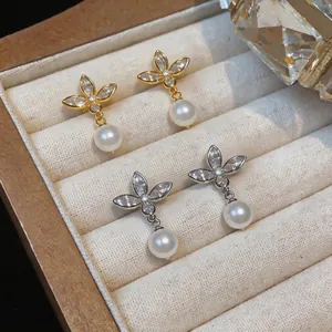 Detailed view of elegant gold and silver butterfly earrings with pearl drops in a box