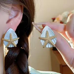 Detailansicht eleganter Ohrstecker mit goldenem Seestern und weißer Tropfenmuschel.