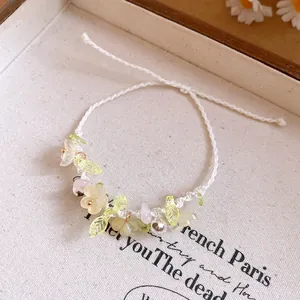Détail macro d'un bracelet à fleurs en résine et cloches sur cordon blanc tressé