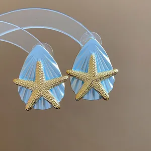 Detailaufnahme von Meeresohrringen mit goldenem Seestern auf hellblauem Muschel.