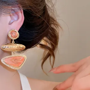 Close-up of geometric orange marbled drop earrings with hammered gold texture