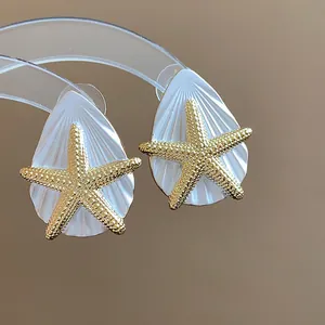 Detaillierte Nahaufnahme eleganter weißer Muschelohrringe mit goldenem Seestern.