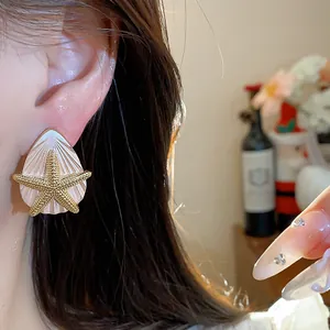 Detailansicht eines eleganten goldenen Seestern- und weißen Muschelohrrings am Ohr des Modells