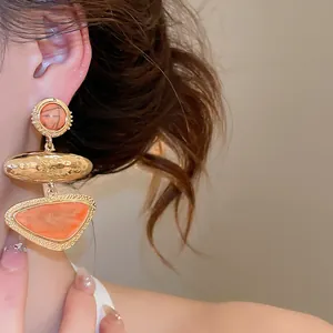 Close-up detail of retro geometric triangle orange earrings displayed on an Asian model