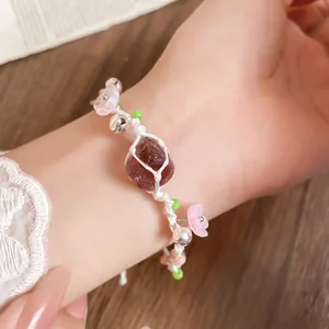 Gros plan détaillé d'un bracelet tissé main avec cristal rouge foncé et fleurs en résine rose