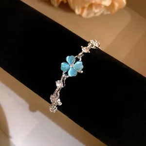 Detail of a silver bracelet featuring blue cat's eye stone and zircon clover charm.