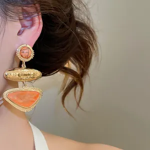 Close-up of vintage geometric triangle earrings with orange marble texture stones on model