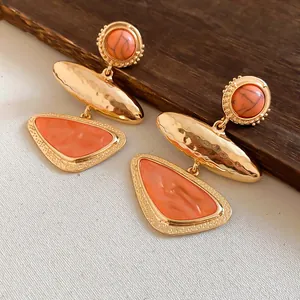 Macro detail of vintage geometric orange triangle earrings with hammered gold texture