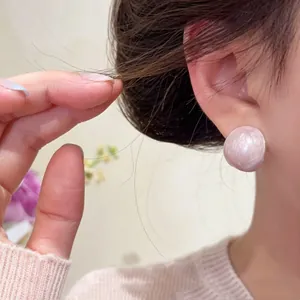 Close-up of model wearing a pale pink enameled stud earring with pearlescent finish