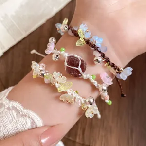 Gros plan de bracelets tissés main avec fleurs en résine, cloches et détails en pierre.