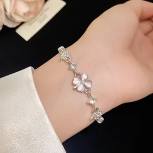 Close-up of a silver four-leaf clover bracelet with pink cat's eye stones on a wrist