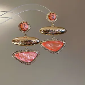 Detailed macro view of vintage geometric dangle earrings featuring hammered gold and coral inlay