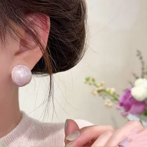 Close-up view of elegant pink oval stud earrings with a pearlescent finish on ear.