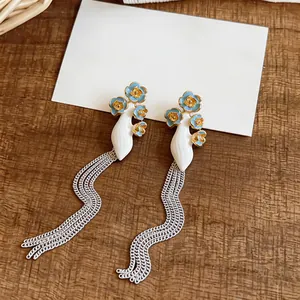 Detail view of long silver tassel earrings featuring blue and gold enamel flowers.
