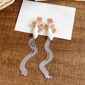 Detailed view of long chain tassel earrings with pink enamel flowers on a white leaf base