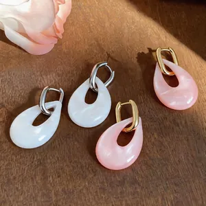 Detailansicht der eleganten rosa und weißen ovalen Harz-Tropfenohrringe auf Holzoberfläche
