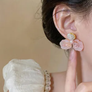 Close-up detail view of a pink flower stud earring with pearl accent on model's ear