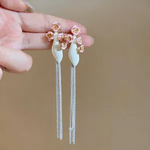 Close-up view of elegant pink flower and white bottle tassel earrings held against a neutral wall