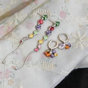 Close-up of colorful zircon tassel and hoop earrings on a delicate floral fabric.