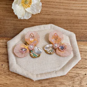 Detail showing French style peach flower earrings with crystal accents on a display pad