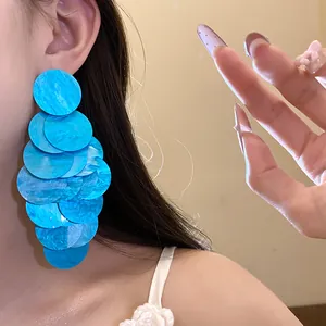 Close-up detail of stylish blue gradient acrylic disc tassel earrings worn on model ear
