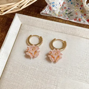 Dettaglio ravvicinato di orecchini a cerchio stile francese con fiori rosa e perle.
