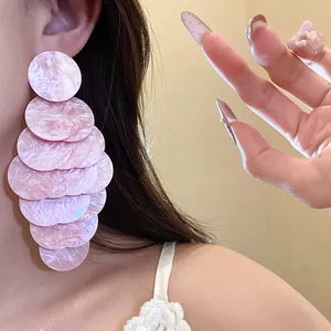 Close-up of pink marbled acrylic layered round disc tassel earrings worn on a person's ear